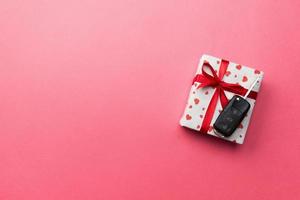 Car key on paper gift box with red ribbon bow and heart on pink table background. Holidays present top view concept photo