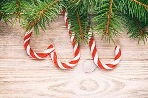Christmas fir tree branches with candy cane on white rustic wooden background with copy space for text. Toned photo