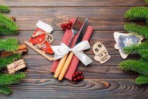 Top view of christmas decorations on wooden background. Close up of fork and knife on napkin tied up with ribbon. New year pattern concept photo