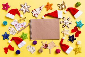 Top view of notebook with Christmas decorations and Santa hats on yellow background. Happy holiday concept photo