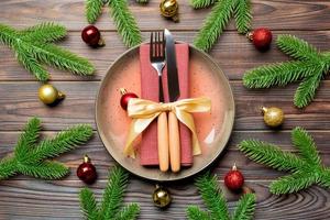 Top view of New Year dinner on festive wooden background. Composition of plate, fork, knife, fir tree and decorations. Merry Christmas concept photo