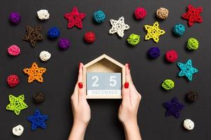 Top view of female hands holding calendar on black background. The twenty fifth of December. Holiday decorations. Christmas time concept photo