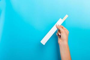 Female hand holding a packet with chopsticks on blue background. Sushi concept with empty space for your idea photo