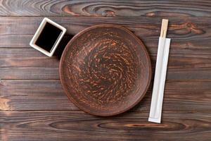 Empty dark vintage round plate with chopsticks for sushi on wooden background. Top view with copy space photo