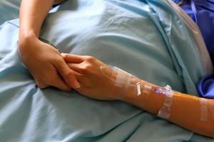 Patient's hands or arm giving the saline solution on bed with copy space. Healthy, Medicine or Medical and injection. People cure sickness and fever at hospital or clinic concept. photo