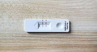 resultado positivo de la prueba mediante el uso de la prueba rápida de antígeno para covid-19 sobre fondo de madera con espacio de copia. control saludable, infección por el virus de la corona, pandemia infecciosa y médica. comprobación inicial de síntomas. foto