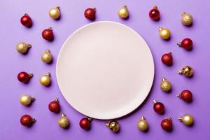 Top view of festive plate with red and golden baubles on colorful background. Christmas decorations and toys. New Year advent concept photo