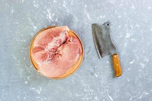 corte crudo de paleta de cerdo a bordo con cuchillo o hacha de cocina. Cuchilla con carne cruda fresca sobre fondo de hormigón gris foto