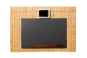 Empty rectangular black slate plate with chopsticks for sushi and soy sauce on yellow bamboo mat background. Top view with copy space for you design photo