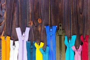 Multicolored zippers are laid out on a wooden table photo