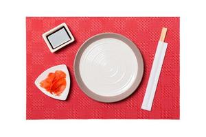 plato blanco redondo vacío con palillos para sushi y salsa de soja, jengibre sobre fondo rojo de sushi. vista superior con espacio de copia para su diseño foto