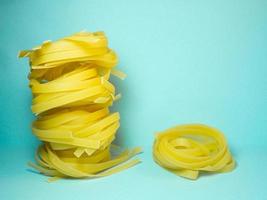 Nests of pasta on a blue background.   Culinary background. Pyramid of noodles. Curled pasta on the table. Uncooked product.   Background from noodles. photo