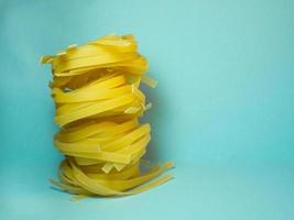 nidos de pasta sobre un fondo azul. fondo culinario. pirámide de fideos. pasta rizada sobre la mesa. producto sin cocinar. fondo de fideos. foto