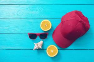 accesorios de verano. gorra, gafas de sol, concha y naranjas sobre fondo de madera azul. vista superior y espacio de copia foto