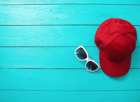 gorra roja y gafas de sol sobre fondo de madera azul. vista superior y espacio de copia. accesorios de verano. foto