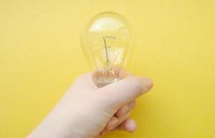 female hand holds a lamp on a yellow background. One lightbulb. Symbol of a new idea. Carry the light metaphor concept. Symbol of shining. photo