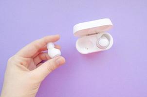 True wireless earbuds. Hand holds white wireless headphones. wireless earbuds on purple background. photo