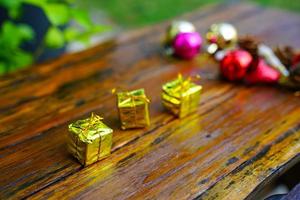 New Year and Christmas gift themed decorations on wooden background, consisting of a golden gift box.  shiny colored balls  Dried pine cones and small bells  free space for design photo