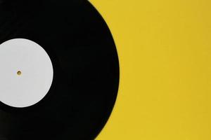 Close up of black old vinyl record play disc vintage on a yellow background with copy space for text. Retro LP history, nostalgia concept. Sound technology for DJ to mix music. Flat lay, top view photo