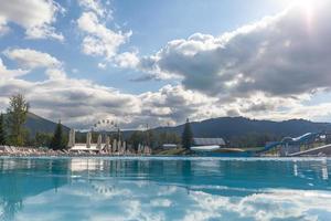 una gran piscina con agua clara al aire libre con el telón de fondo de la hermosa naturaleza. una piscina con toboganes, tumbonas en el lugar, un buen lugar para relajarse con familiares y amigos. foto