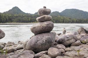 A pyramid of bare stones stacked on top of each other. Stones stacked in the shape of a pyramid on the riverbank against the background of mountains as balance and balance in nature, Zen, Buddhism. photo