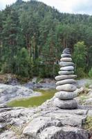 A pyramid of bare stones stacked on top of each other. Stones stacked in the shape of a pyramid on the riverbank against the background of mountains as balance and balance in nature, Zen, Buddhism. photo