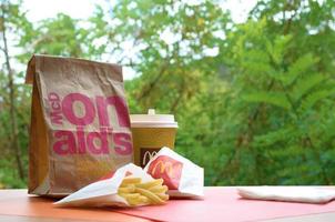 KHARKOV, UKRAINE - MAY 12, 2022 McDonald's take away paper bag and junk food on wooden table outdoors photo