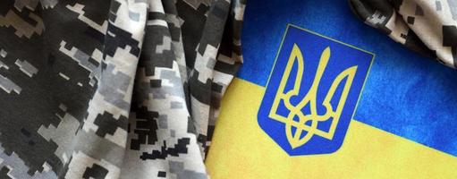 Ukrainian flag and coat of arms with fabric with texture of pixeled camouflage. Cloth with camo pattern in grey, brown and green pixel shapes with Ukrainian trident sign photo