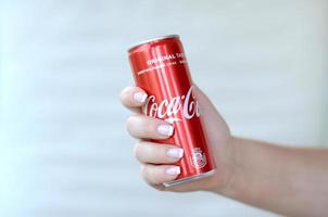 Jarkov. ucrania - 2 de mayo de 2022 mano femenina sostiene una lata de coca-cola roja sobre fondo de pared blanca foto