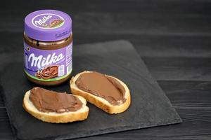 KHARKOV. UKRAINE - MAY 2, 2022 Can of Milka sweetened hazelnut cocoa spread with classical lilac color design on black table photo