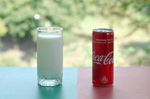 KHARKOV. UKRAINE - MAY 2, 2022 Coca cola red tin can and cup of fresh milk on colored surface photo