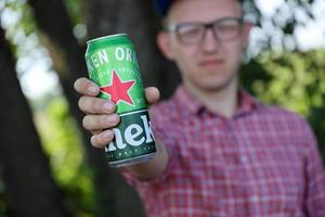 KHARKOV, UKRAINE - JULY 31, 2022 Man with green tin can of Heineken lager beer produced by the Dutch brewing company Heineken N.V. photo