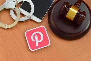 KHARKOV, UKRAINE - MAY 12, 2022 Pinterest paper logo lies with wooden judge gavel, smartphone and handcuffs. Entertainment lawsuit concept photo