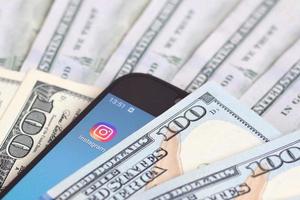 kharkov, ucrania - 12 de mayo de 2022 pantalla de teléfono inteligente con aplicación de instagram y muchos billetes de cien dólares. concepto de negocios y redes sociales foto