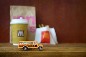 KHARKOV, UKRAINE - MAY 12, 2022 Small school bus and McDonald's junk food on wooden table photo