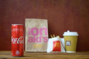 KHARKOV, UKRAINE - MAY 12, 2022 McDonald's take away paper bag and french fries with coca cola can on wooden table photo