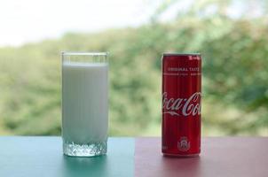 KHARKOV. UKRAINE - MAY 2, 2022 Coca cola red tin can and cup of fresh milk on colored surface photo
