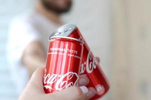 KHARKOV. UKRAINE - MAY 2, 2022 Happy young man raise Coca-Cola tin can with female friend in garage interior photo