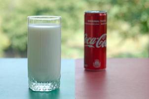 KHARKOV. UKRAINE - MAY 2, 2022 Coca cola red tin can and cup of fresh milk on colored surface photo