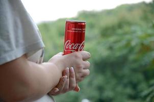 Jarkov. ucrania - 2 de mayo de 2022 una mujer caucásica sostiene una lata de coca-cola roja con fondo de jardín verde foto