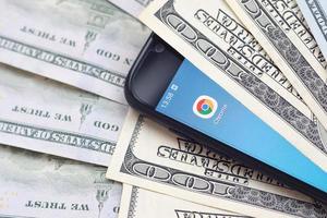 KHARKOV, UKRAINE - MAY 3, 2022 Smartphone screen with Google chrome app and lot of hundred dollar bills. Business and social networking concept photo