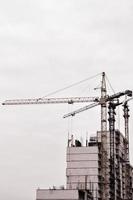 Working tall cranes inside place for with tall buildings under construction against a clear blue sky. Crane and building working progress. Retro tone photo