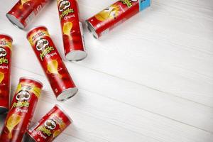 KHARKOV, UKRAINE - MAY 5, 2022 Pringles original flavour. Cardboard tube cans with Pringles potato chips on white table. Pringles is a brand of potato snack chips owned by the Kellogg Company photo