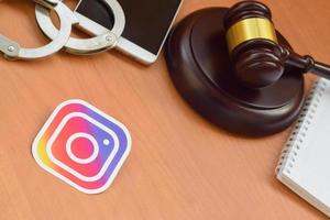 KHARKOV, UKRAINE - MAY 5, 2022 Instagram paper logo lies with wooden judge gavel, smartphone and handcuffs. Entertainment lawsuit concept photo