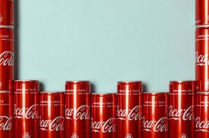KHARKOV. UKRAINE - MAY 2, 2022 Flat lay shot carbonated red drink tin cans Coca Cola laying on pastel blue background photo