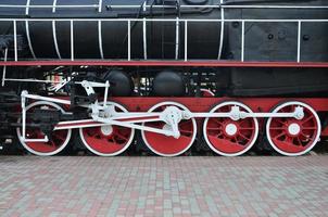 ruedas de la vieja locomotora de vapor negra de la época soviética. el lado de la locomotora con elementos de la tecnología giratoria de trenes antiguos foto