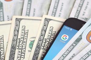 KHARKOV, UKRAINE - MAY 12, 2022 Smartphone screen with Google app and lot of hundred dollar bills. Business and social networking concept photo