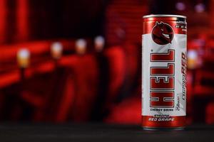 KHARKOV, UKRAINE - MAY 12, 2022 Hell energy drink can on black wooden table with red interior background photo