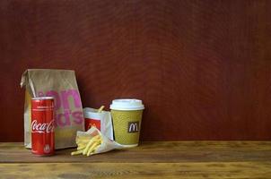 KHARKOV, UKRAINE - MAY 12, 2022 McDonald's take away paper bag and french fries with coca cola can on wooden table photo