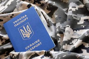 Ukrainian foreign passport on fabric with texture of military pixeled camouflage. Cloth with camo pattern in grey, brown and green pixel shapes and Ukrainian ID photo